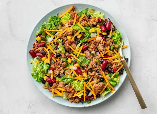 A vibrant taco salad featuring black beans, corn, and a generous topping of shredded cheese healthy lunch suggestions