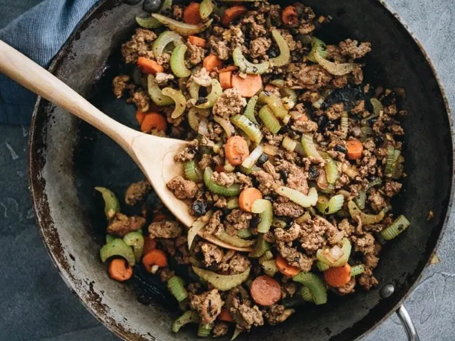 A skillet containing a mixture of ground beef and colorful vegetables, sizzling and ready for a delicious meal Cook with Ground Beef