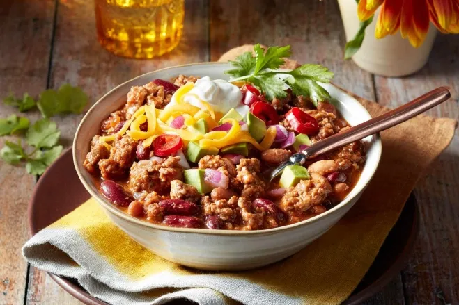 A bowl of chili con carne, featuring rich, hearty beans and meat, garnished with fresh herbs and spices chop meat dinner ideas