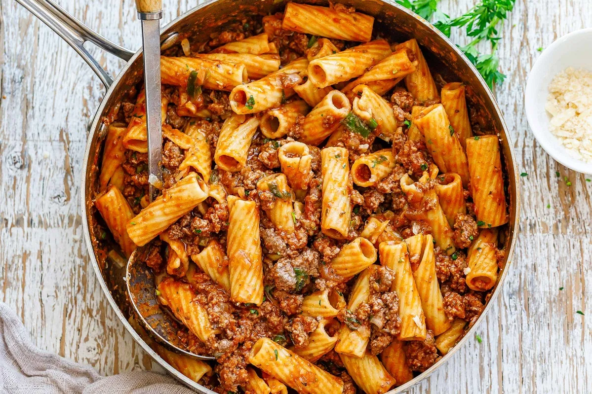 A pan filled with pasta topped with meat and melted cheese, showcasing a delicious and hearty meal ground meat dishes