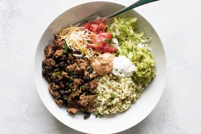  A vibrant Mexican rice bowl featuring ground beef, black beans, and fresh shredded lettuce, served in a colorful dish meals to cook with ground beef