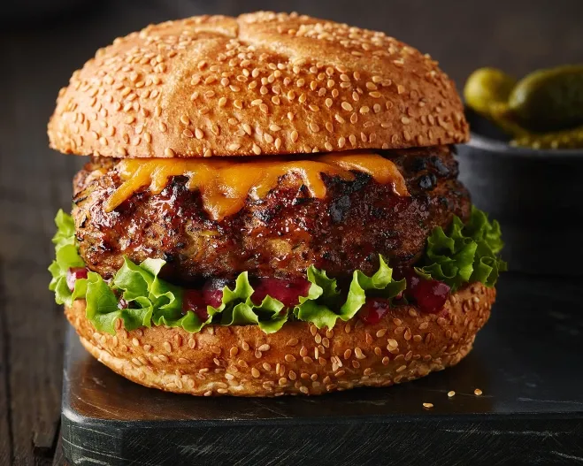 A delicious hamburger topped with cheese and fresh lettuce, elegantly presented on a sleek black plate recipes with groundbeef