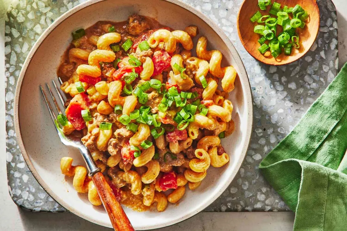 A bowl of pasta featuring meat and vegetables, garnished with fresh green onions for added flavor and color dinner meals with ground beef