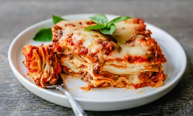 A serving of lasagna on a plate accompanied by a fork, showcasing layers of pasta, cheese, and sauce dinner meals with ground beef