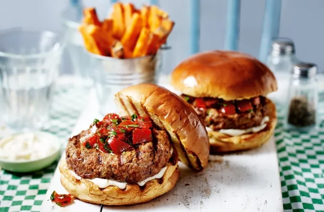 Two burgers topped with tomato and cheese placed on a wooden cutting board, ready to be served meals to cook with ground beef