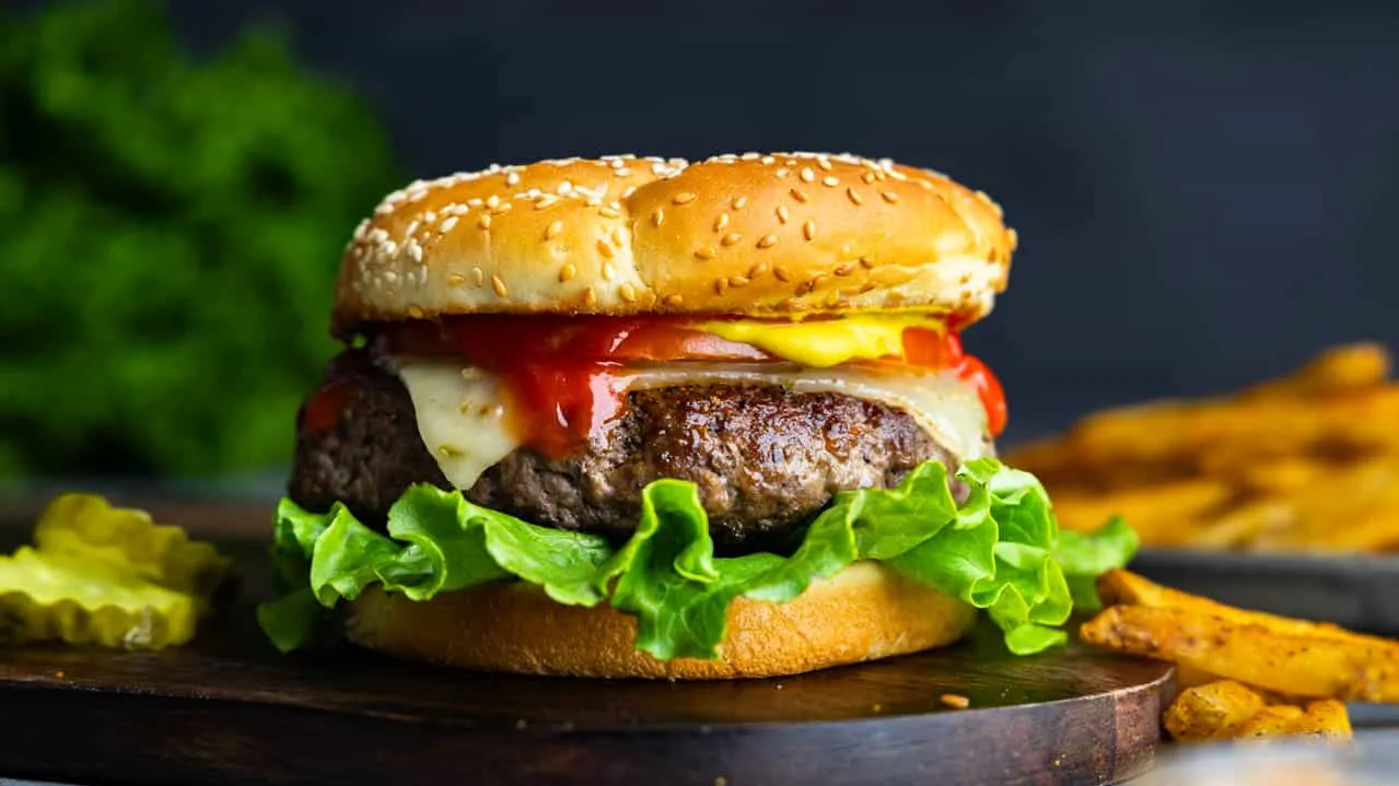 1. A delicious hamburger topped with cheese, lettuce, and tomato, presented on a rustic wooden cutting board ground beef