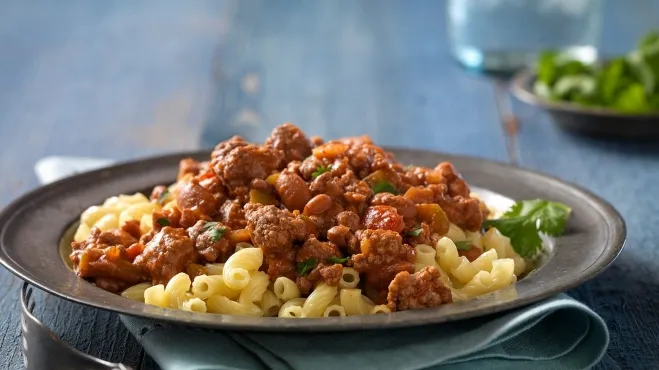 A hearty bowl of chili mac and cheese, featuring pasta, chili, and melted cheese, garnished with fresh herbs ground meat dishes