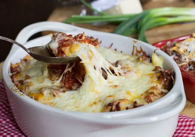 A serving of baked spaghetti topped with meatballs, garnished with herbs and melted cheese, presented in a white dish ground beef dishes for dinner