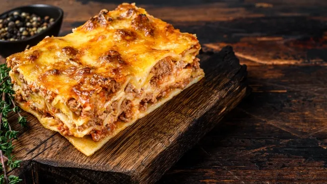 1. A delicious piece of lasagna served on a rustic wooden board, showcasing layers of pasta, cheese, and sauce food recipes with ground beef