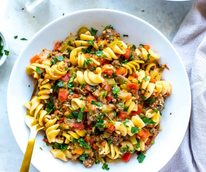 A bowl of pasta featuring a mix of meat and colorful vegetables, showcasing a hearty and appetizing meal Cook with Ground Beef 