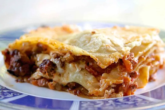  A slice of lasagna served on a white plate, showcasing layers of pasta, cheese, and rich tomato sauce ground meat dishes