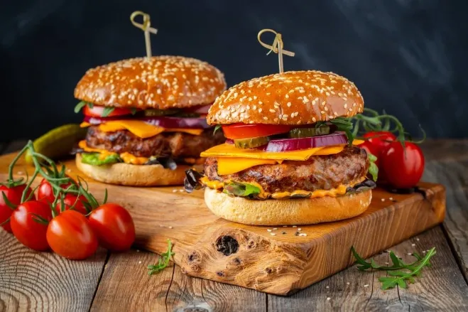 Two cheeseburgers with fresh tomatoes displayed on a wooden cutting board, highlighting their appetizing appearance dinner with hamburger meat ideas