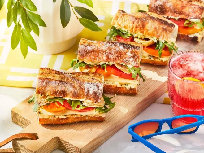  A wooden cutting board displaying an assortment of sandwiches alongside refreshing drinks lunchtime ideas